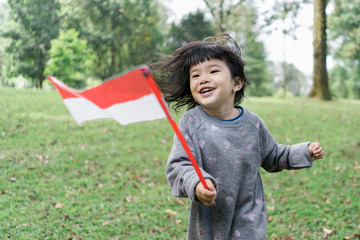 asian little girl holding a stick of Indonesian flag when look at at camera with toothy