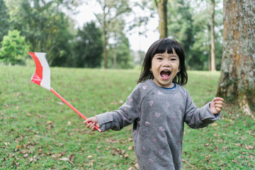 little asian girl flapping indonesia national flag with smile when walking in the park