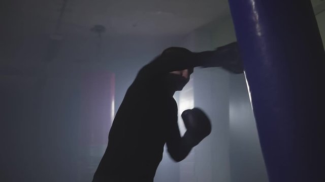 Kickboxer punching in smoky studio. Muay thai fighter training with punching bag on dark background
