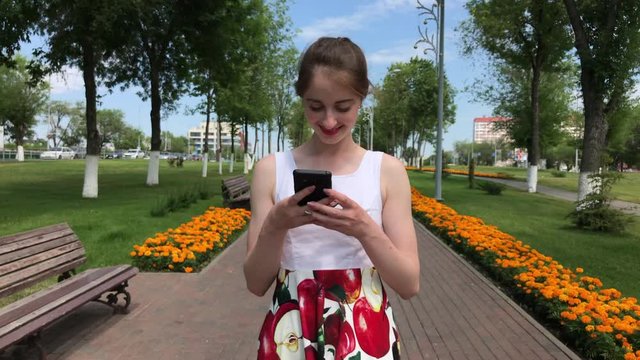 Young beautiful woman calling by phome in flowers dress walking in summer park