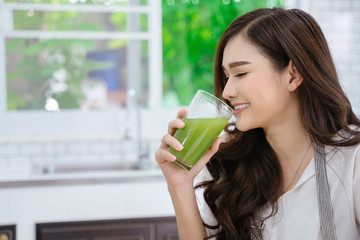 young girl drinking green cocktail with a straw.Woman drinking a homemade green detox juice. texting on her phone while sitting in her kitchen table 