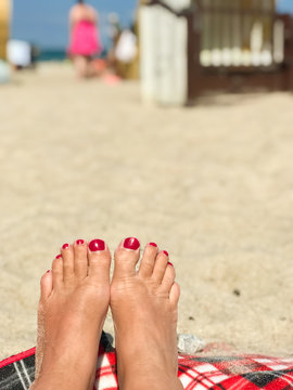 Woman feet with red nail polish at the beach, in the background beach chairs and blue sky