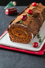 Buche de Noel. Traditional Christmas dessert, Christmas yule log cake with chocolate cream, cranberry. On stone gray background with Christmas tree branches.
