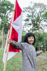 asian little girl flapping Indonesian flag with spirit in the park