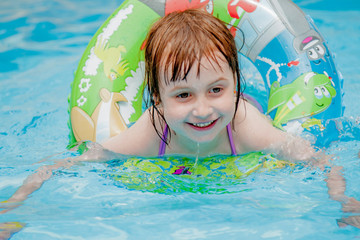 Funny facial expression of happy cute little child girl playing with ring in swimming pool. Kids...
