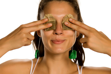 Young smiling woman posing with tea bags on her eyes on white background