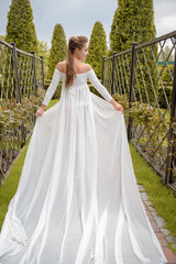Fototapeta premium Princess in a vintage white dress. Walk along the picturesque summer field at sunset. A long train of white skirt fluttered on the run.
