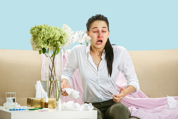 Young woman suffering from hausehold dust or seasonal allergy. Sneezing in the napkin and sitting...