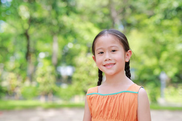 Portrait of happy little Asian child in green garden with looking at camera. Close up smiling kid girl in summer park.
