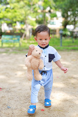 Happy toddler boy walking outside with holding teddy bear in the park outdoor.