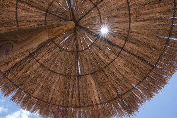 Pretty sun flare viewed through a straw parasol against a bright blue sky,