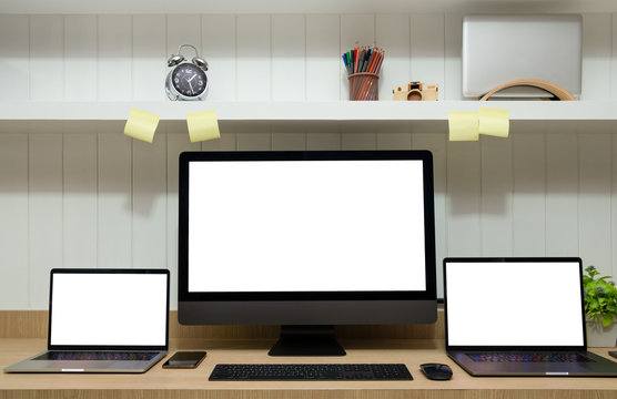 Mockup image of three computers with blank white screen background on wood table top, business concept. Mockup design with copy space.