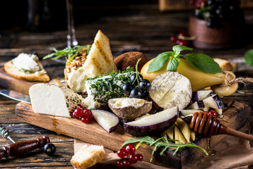 Cheese appetizer selection. Red currant, honey, basil, grapes and nuts on rustic wooden board over wooden concrete backdrop, top view. Belper Knolle, goat cheese, Scamorza. Cheese board, cheese plate