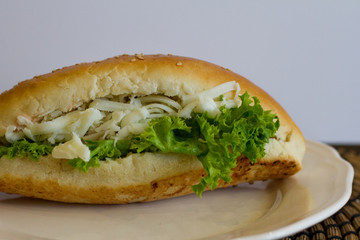 fresh sandwich with ham, cheese, bacon, tomato, salad, cucumber and onion on a white plate. Quick snack and food. Juicy hamburger. Baguette with vegetables.