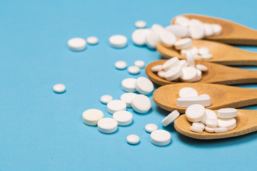 Assorted pharmaceutical medicine pills, tablets and capsules on wooden spoon. blue background