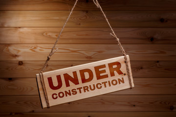 Wooden signboard with the words UNDER CONSTRUCTION on a rough rope on a beautiful wooden background