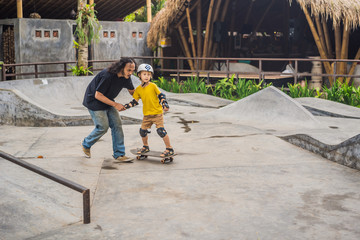 Athletic boy learns to skateboard with a trainer in a skate park. Children education, sports