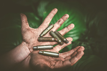 Obraz premium empty shot ammunition and the whole ammunition in dirty children's hands against a background of green foliage