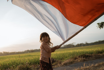 Little girl pride flapping Indonesian flag with happiness in the rice field