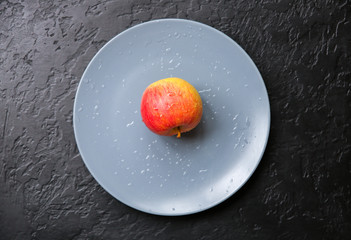 An apple lying on the grey plate. Still life photo. Black background.