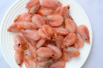 Frozen boiled shrimps lie on a white plate. Shrimps in ice glaze are defrosted on a plate.