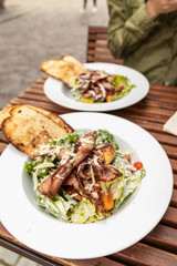 Close up of hands holding Caesar salad in restaurant. Tasty salad on white wooden table in cafe