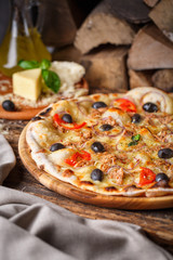 Pizza with fish, olives, onions and tomatoes on the background of firewood