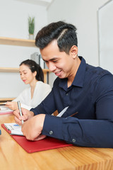Asian smiling businessman sitting at the table and working with business documents with businesswoman working near by him at office