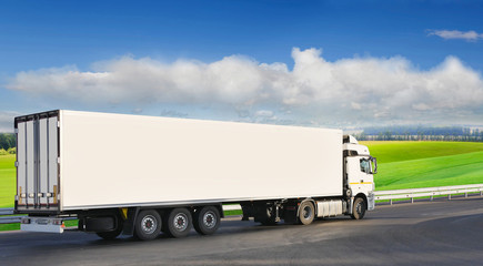 White trailer on the highway, against the background of a green field.