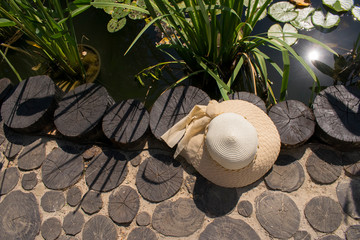 Romantic straw hat with ribbon the on a wooden walkway near the pond. Sun glare on the water in the pond, bright sunny summer day. Summer holidays background.