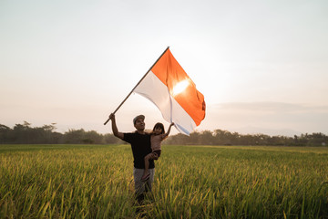 asian young father with daughter flapping Indonesian flag with spirit in the rice field