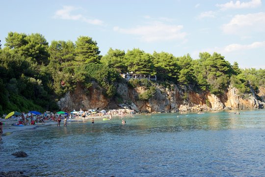 Skala beach in the afternoon at summer with swimmers and tourists. Background view of the green pine trees forest on the cliff. Skala is a sandy exotic beach at the region of Preveza in Epirus, Greece