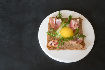 Galette bretonne  with fried eggs, arugula and bacon on a black background.