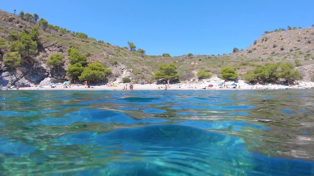 Spain, Mediterranean beach with tourists in summer seen from water surface and moving camera down underwater to see seagrass underwater, Costa Brava, Roses, Cala Murtra, Catalonia