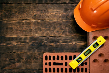 Construction concept background with a copy space. Hardhat, bricks and bubble level on a brown wooden table background.