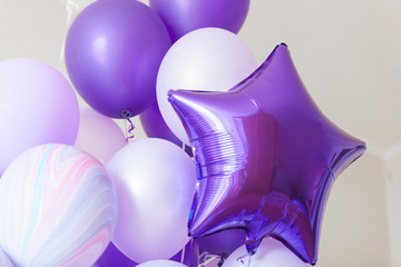 Flying round lilac and deep purple star balloons on light gray background while celebration. Birthday background with ballons.