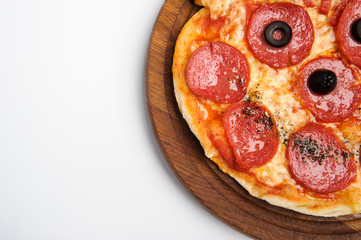 Delicious pizza with tomatoes and pepperoni - thin pastry crust at wooden round desk isolated at white background