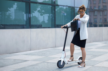 Young and beautiful businesswoman rides electric scooter