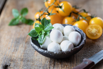 Mozzarella cheese, yellow tomatoes and basil in a ceramic bowl on a wooden board. Caprese salad ingredients. Selective focus