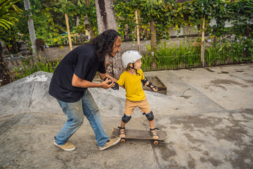 Athletic boy learns to skateboard with a trainer in a skate park. Children education, sports