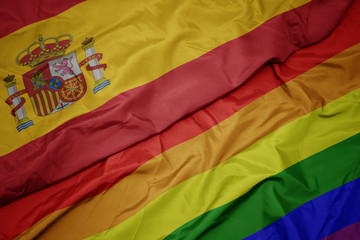 waving colorful gay rainbow flag and national flag of spain.