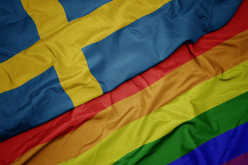 waving colorful gay rainbow flag and national flag of sweden.