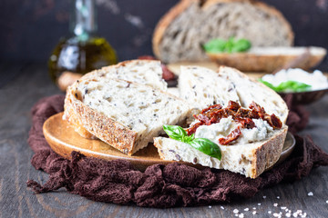 Bread slices with ricotta cheese, sun dried tomatoes and basil served on wooden cutting board. Bruschetta with ricotta cheese, dried tomatoes and basil. 