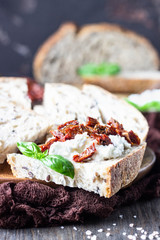 Bread slices with ricotta cheese, sun dried tomatoes and basil served on wooden cutting board. Bruschetta with ricotta cheese, dried tomatoes and basil. 