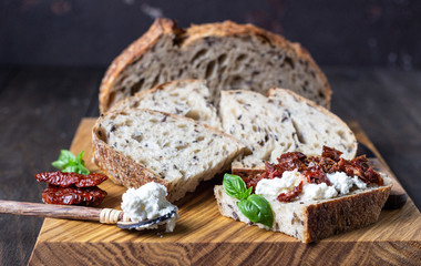 Bread slices with ricotta cheese, sun dried tomatoes and basil served on wooden cutting board. Bruschetta with ricotta cheese, dried tomatoes and basil. 