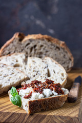 Bread slices with ricotta cheese, sun dried tomatoes and basil served on wooden cutting board. Bruschetta with ricotta cheese, dried tomatoes and basil. 