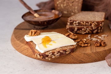 Sliced rye bread on cutting board with camembert cheese and honey. Whole grain rye bread with seeds. Breakfast.