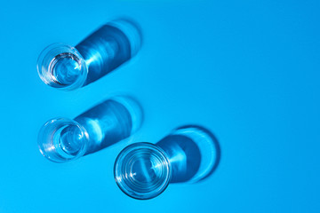Three glasses filled with clear water on a blue background. Top view.