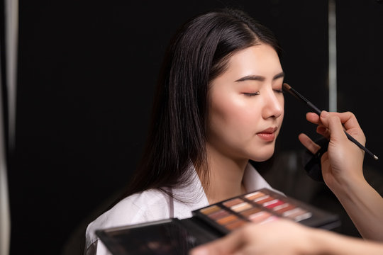 Beautiful young asian woman and professional makeup artists applies eye shadow. Beautiful woman face. Perfect makeup