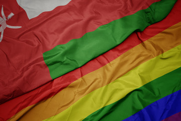 waving colorful gay rainbow flag and national flag of oman.